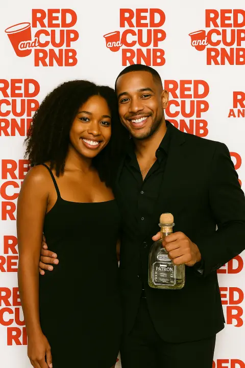 Couple in black outfits posing with a bottle at a Red Cup R&B backdrop